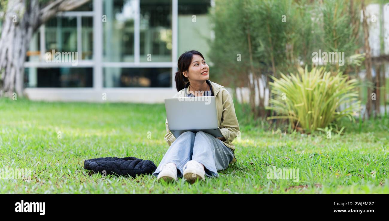 Junge asiatische Studentin sitzt und benutzt Laptop an der Universität vor dem Klassenzimmer. Bildung, Schulkonzept Stockfoto