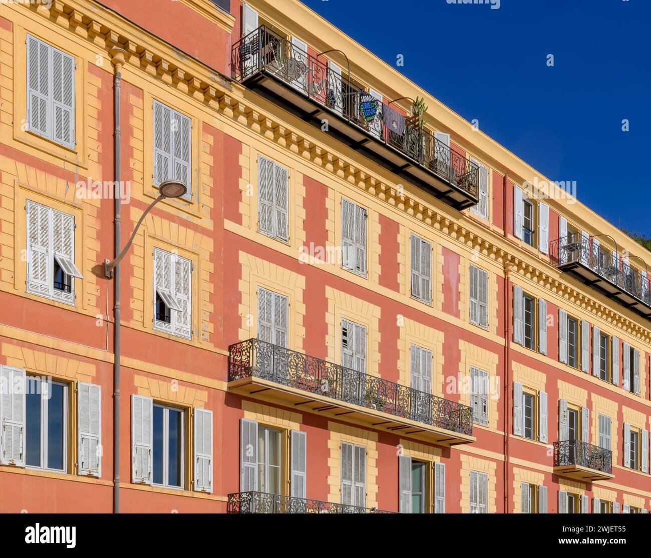 Schicke Apartments an der Küste von Nizza, an der französischen Riviera - Cote d'Azur, Frankreich. Herrliche Ockerfarben mit blau-grauen Fensterläden. Stockfoto