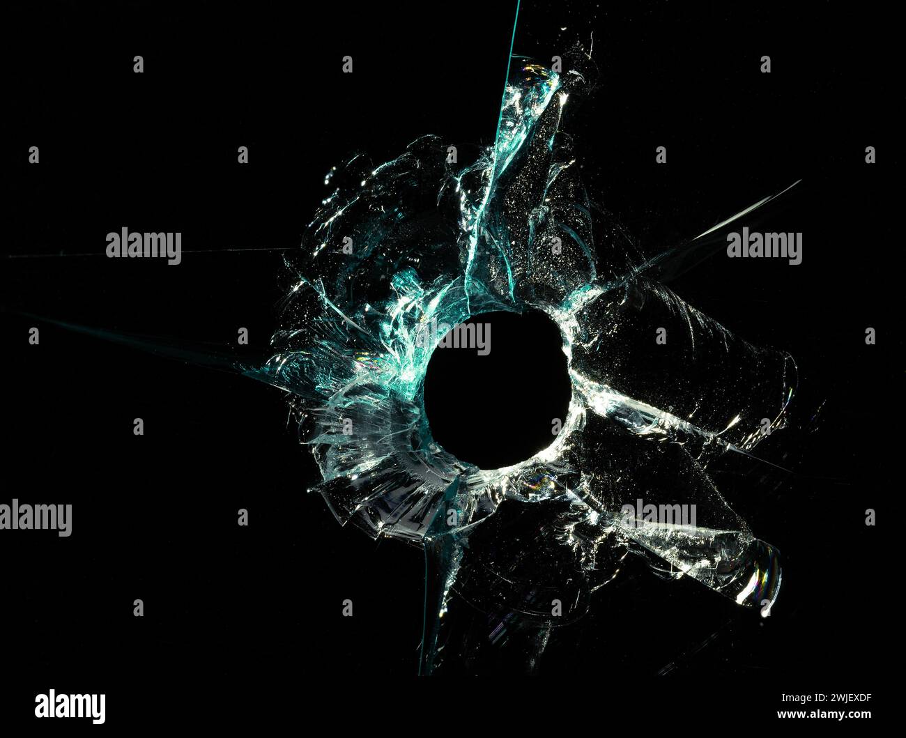 Gebrochene Glasstruktur mit Kugelloch und grünen Rissen auf schwarzem Hintergrund. Makroaufnahme. Stockfoto