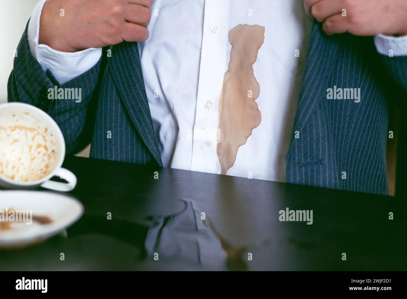 Ein Mann in einem Anzug verschüttete Kaffee auf ein weißes Hemd im Café. Dreckiger brauner Kaffeefleck auf der Kleidung. Daily Life Flin Concept. Stockfoto