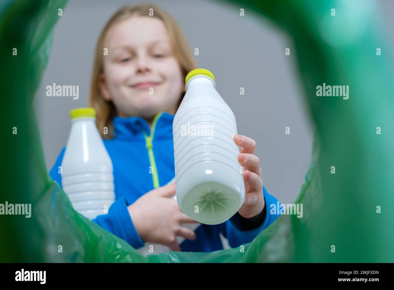 Niedriger Blickwinkel: Ein Kind sortiert den Papierkorb aus Kunststoff zu Hause. Entsorgung von Milchflaschenprodukten. Nachhaltige und umweltbewusste Gesellschaft Stockfoto