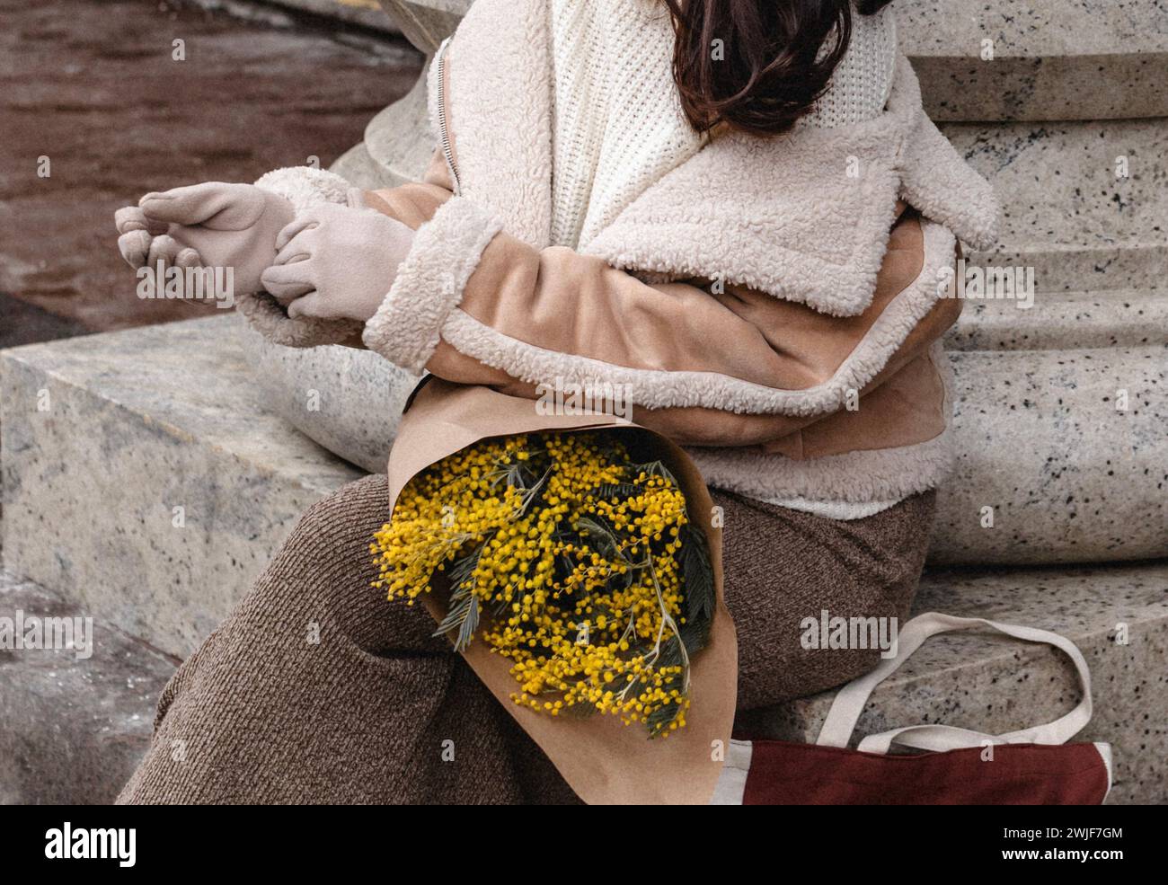 Modische Details aus beigefarbener warmer Jacke, braunem Rock und einem Blumenstrauß frischer Mimosa. Stylischer Winter-Look Stockfoto
