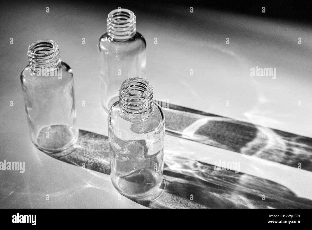 Leere Glasflaschen aus der Unterkosmetik werfen einen Schatten auf einen weißen Tisch Stockfoto