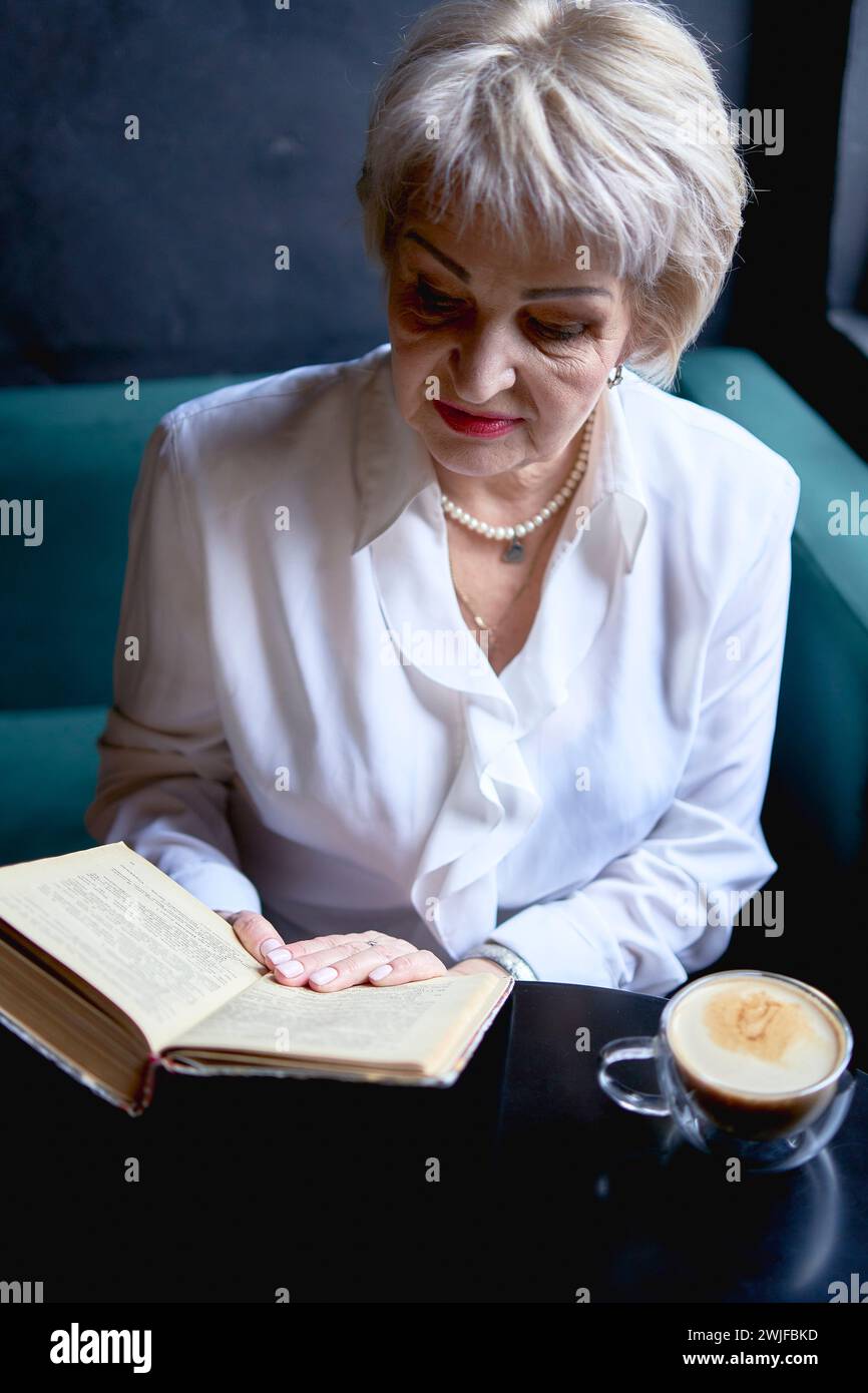 Eine ältere Frau liest ein Buch in einem Café und trinkt Kaffee Stockfoto