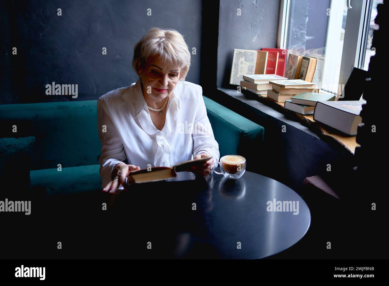 Eine ältere Frau liest ein Buch in einem Café und trinkt Kaffee Stockfoto