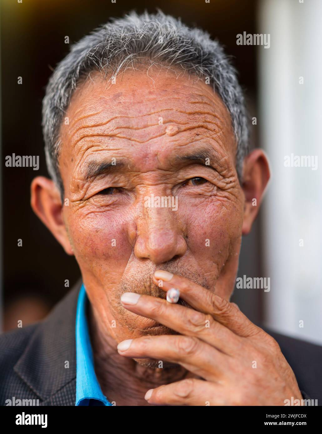 Ein Porträt eines älteren Ladakhi-Mannes, der eine Zigarette raucht und in die Kamera schaut. Stockfoto
