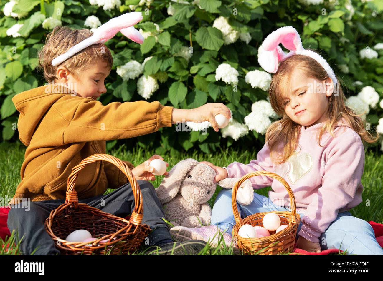 Kleiner Junge und Mädchen in Hasenohren mit Körben mit Eiern an traditionellen Osterferien an sonnigen Tagen Stockfoto