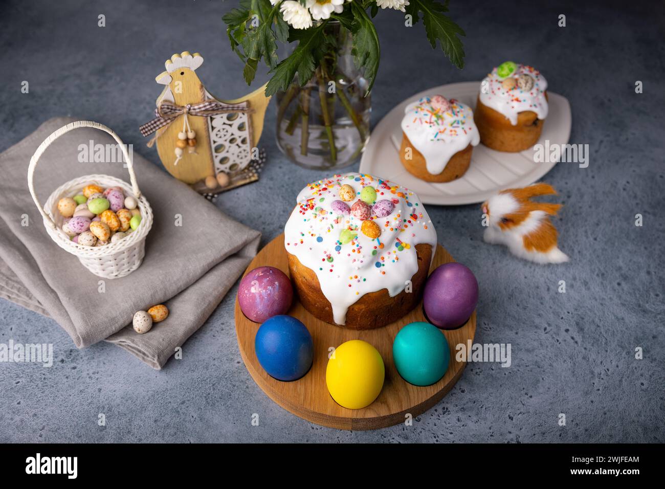 Osterkulich mit kandierten Früchten in weißer Glasur mit bunten Streuseln und bemalten Eiern. Traditionelles Ostergebäck. Osterferien. Nahaufnahme, wählen Sie Stockfoto