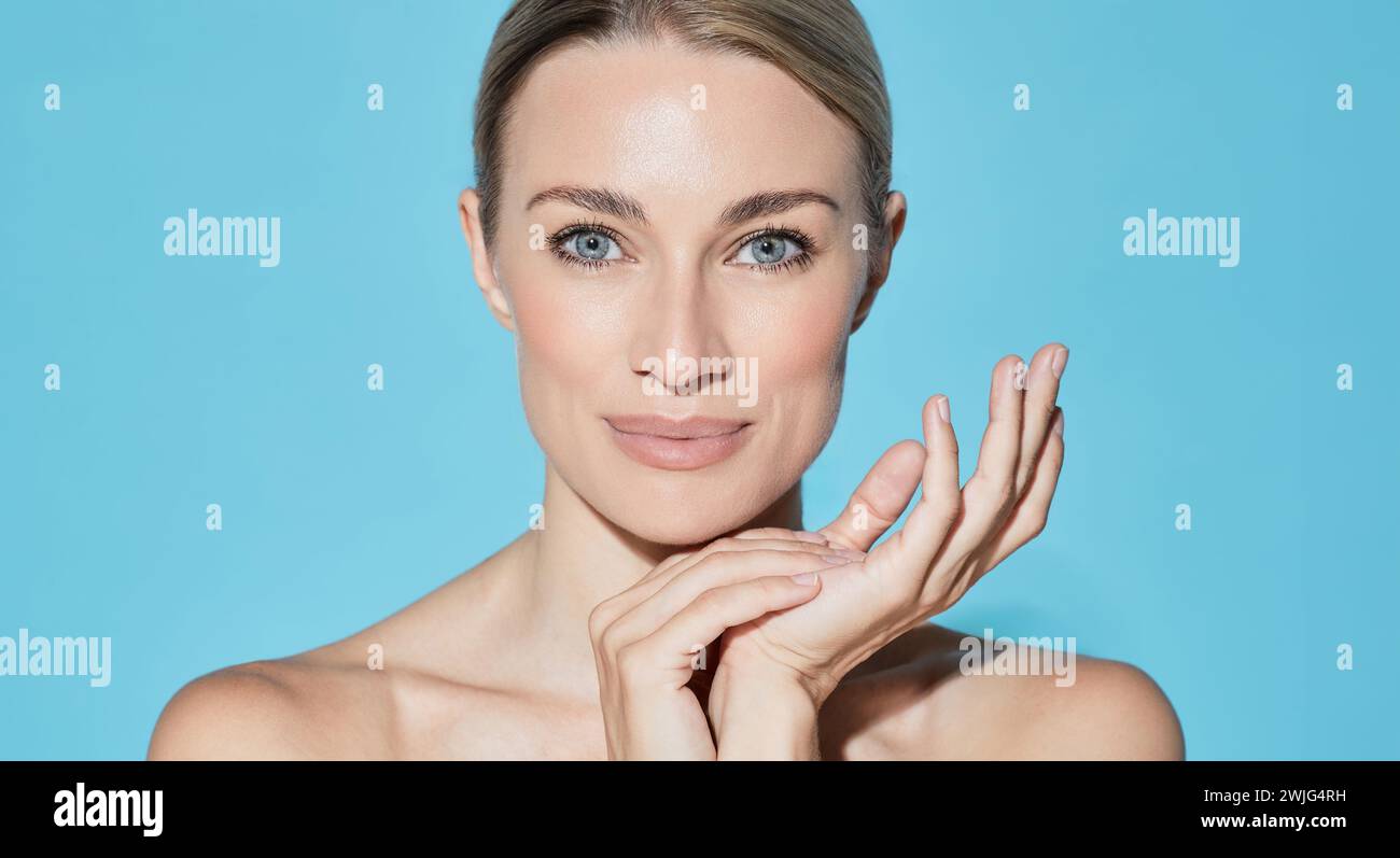 Schöne kaukasische Frau mit gesunder, feuchtigkeitsspendender Gesichtshaut, auf blauem Hintergrund während der Hautpflege. Hautpflege, hohe Qualität Stockfoto