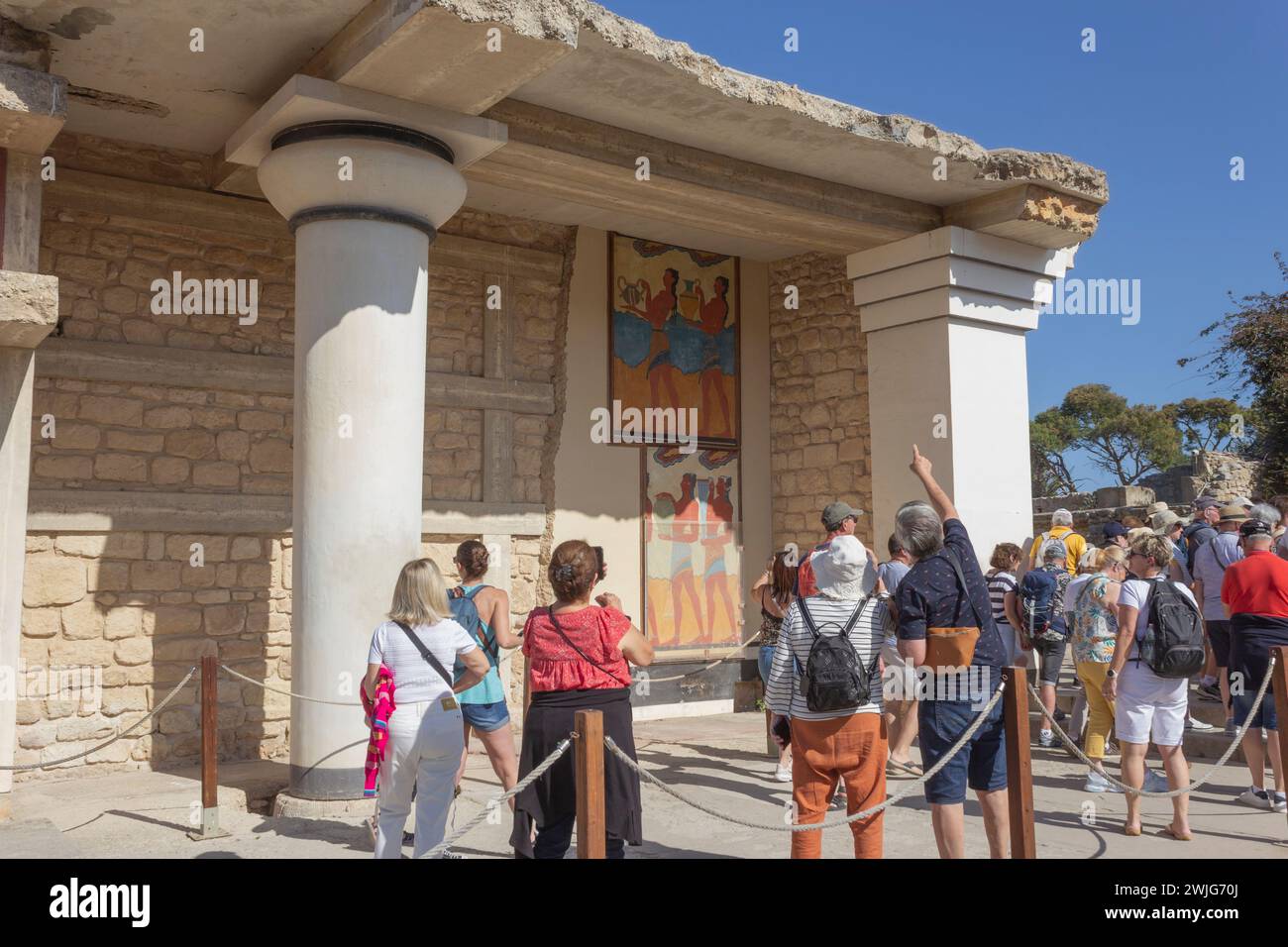 Palast von Minos, Knossos, Kreta, Griechenland. Eine Gruppe von Touristen, die das Fresko der „Prozession“ im südlichen Propylaeum bewundern. Stockfoto