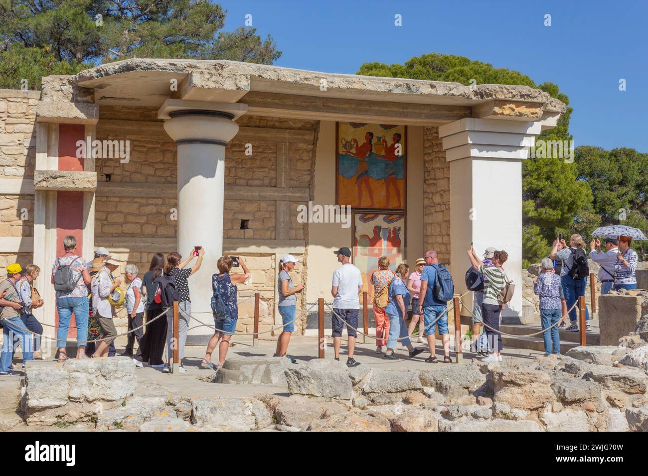 Palast von Minos, Knossos, Kreta, Griechenland. Eine Gruppe von Touristen, die das Fresko der „Prozession“ im südlichen Propylaeum bewundern. Stockfoto