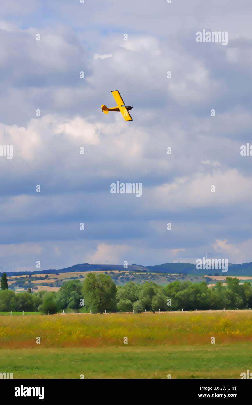 Gelbes einmotoriges Flugzeug manövriert nahe am Boden mit bewölktem Himmel im Hintergrund Stockfoto