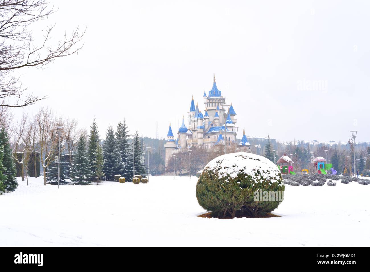 Blaues altes Schloss unter Schnee hinter Büschen und Bäumen im Winter Stockfoto