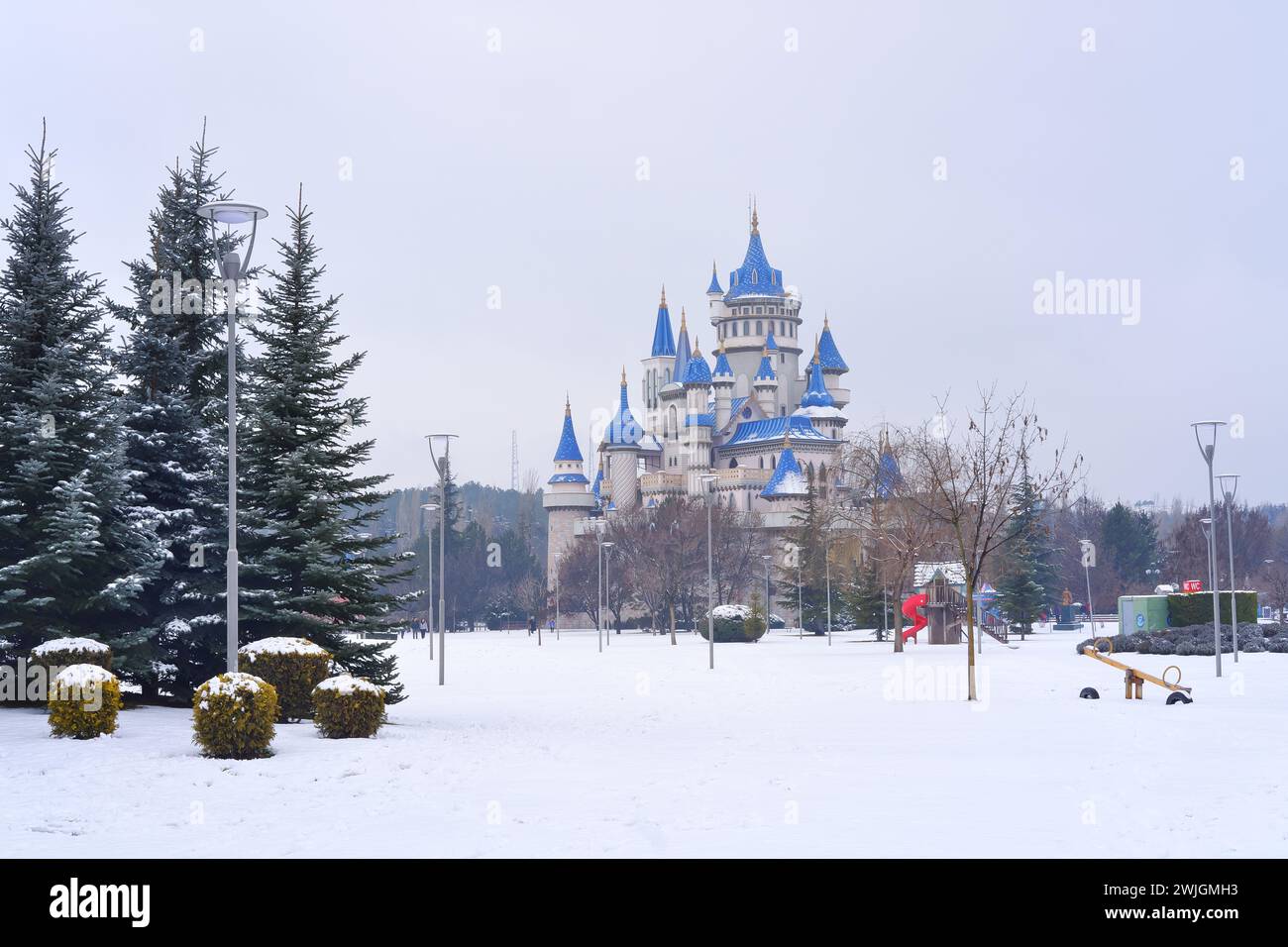 Blaues altes Schloss unter Schnee hinter Büschen und Bäumen im Winter Stockfoto