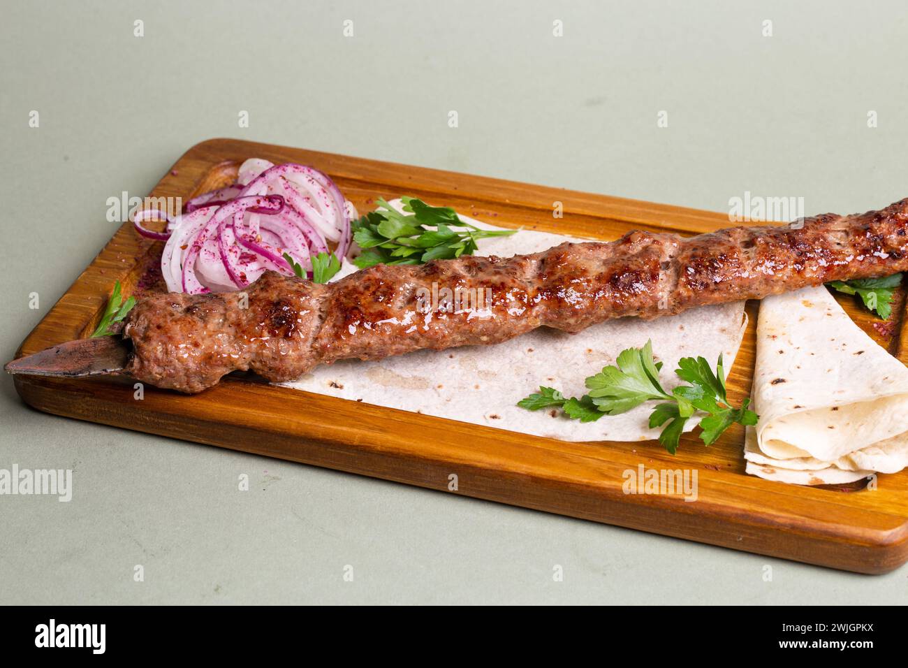 Köstlicher Hähnchenshish Kebab serviert auf einem Holzbrett mit Zwiebelringen und Petersilie. Stillen Sie Ihren Appetit mit diesem geschmackvollen Gericht. Stockfoto
