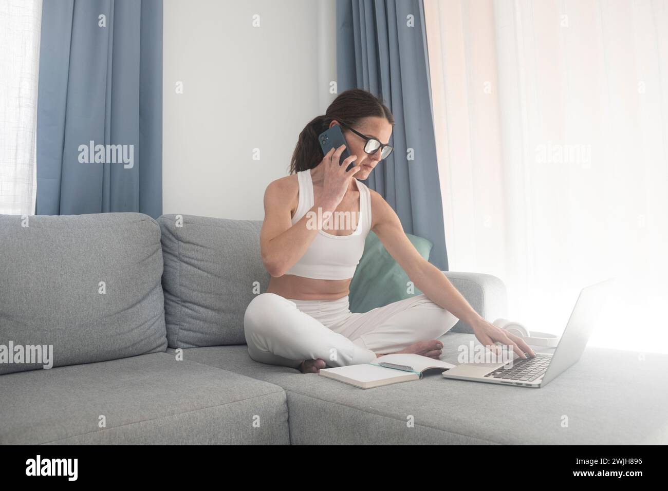 Beschäftigte Frau, die von zu Hause aus mit ihrem Handy und Laptop arbeitet Stockfoto