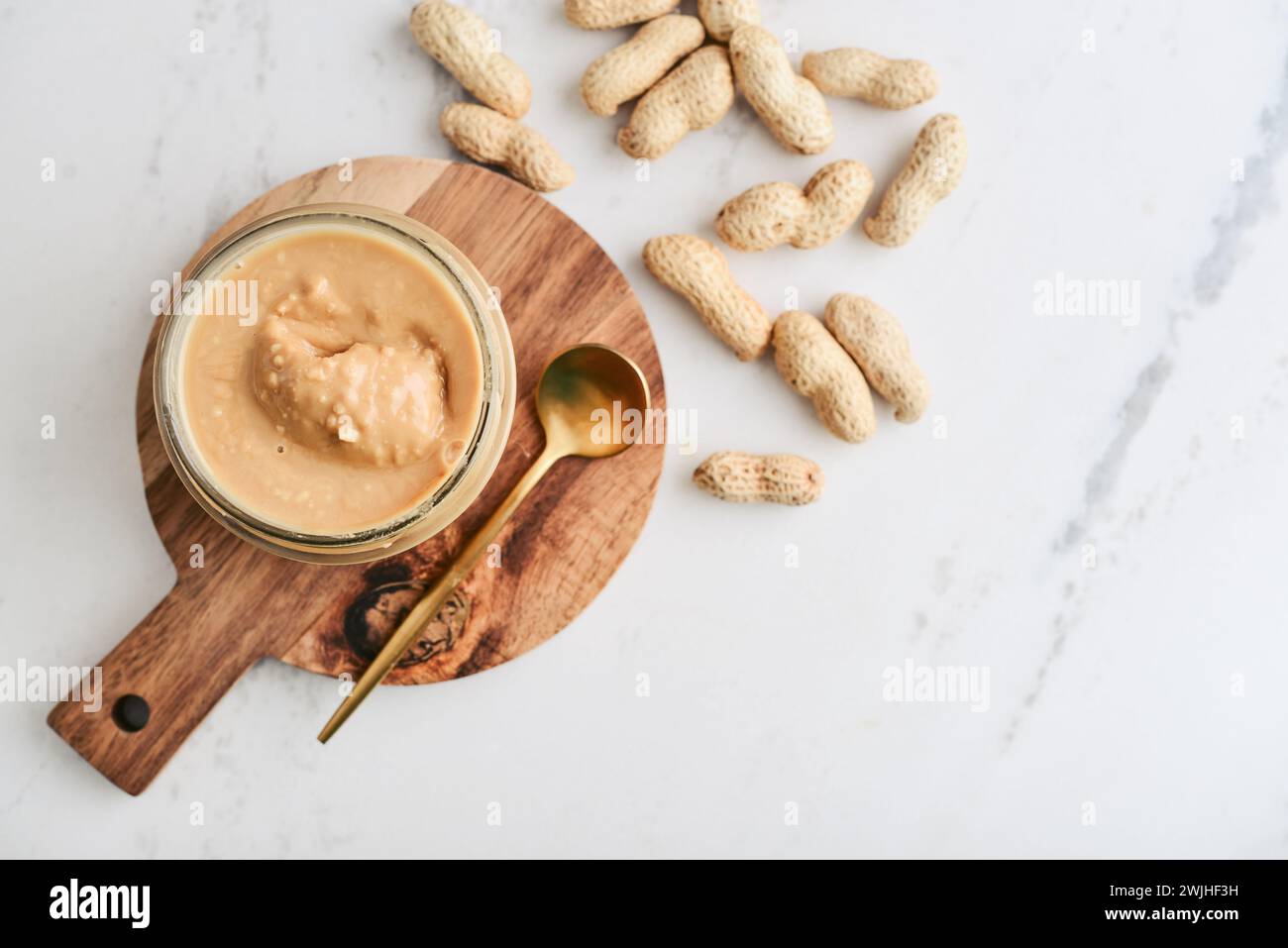 Cremige und glatte Erdnussbutter im Glas Erdnüsse in Schale auf Marmortisch. Natürliche Ernährung und Bio-Lebensmittel. Stockfoto