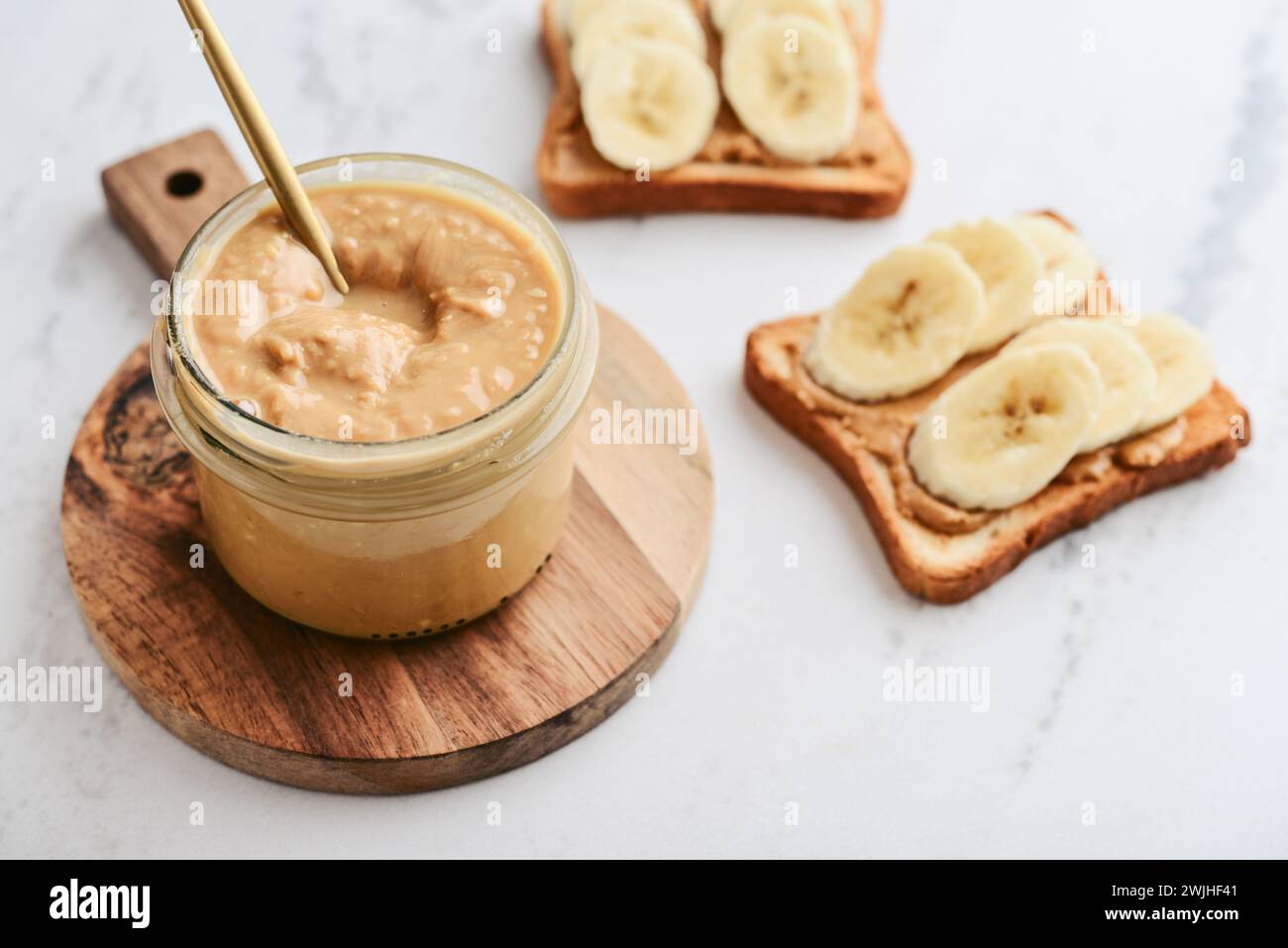 Cremige und glatte Erdnussbutter im Glas Erdnüsse in Schale auf Marmortisch. Natürliche Ernährung und Bio-Lebensmittel. Stockfoto