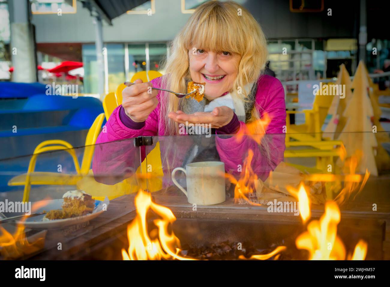 Frau genießt Kaffee und isst Karottenkuchen draußen am warmen Feuer im Winter Stockfoto