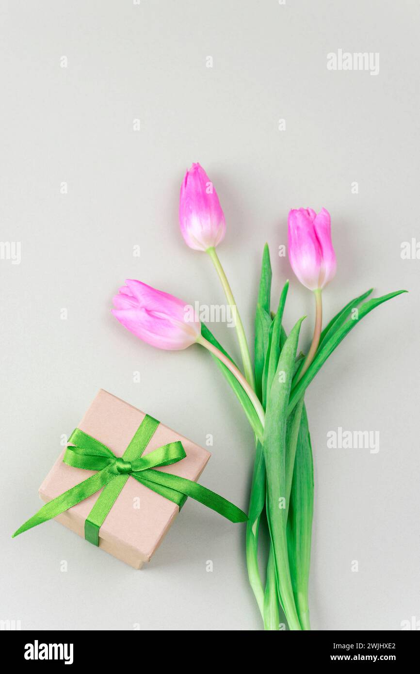 Geschenkbox und Blumenstrauß aus rosa Tulpen auf hellgrünem Hintergrund. Frauentag, Muttertag, Frühlingskonzept. Draufsicht, flach. Stockfoto