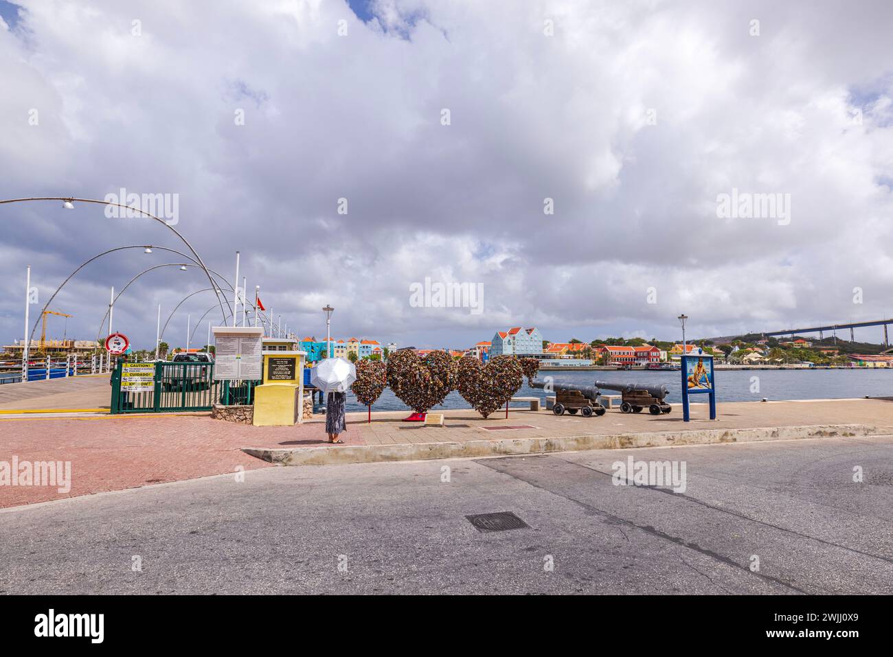 Blick auf die Wahrzeichen entlang der St. Anna Bay Uferpromenade mit Queen Emma Bridge vor dem Hintergrund des bewölkten Himmels. Curacao. Willemstad. Stockfoto