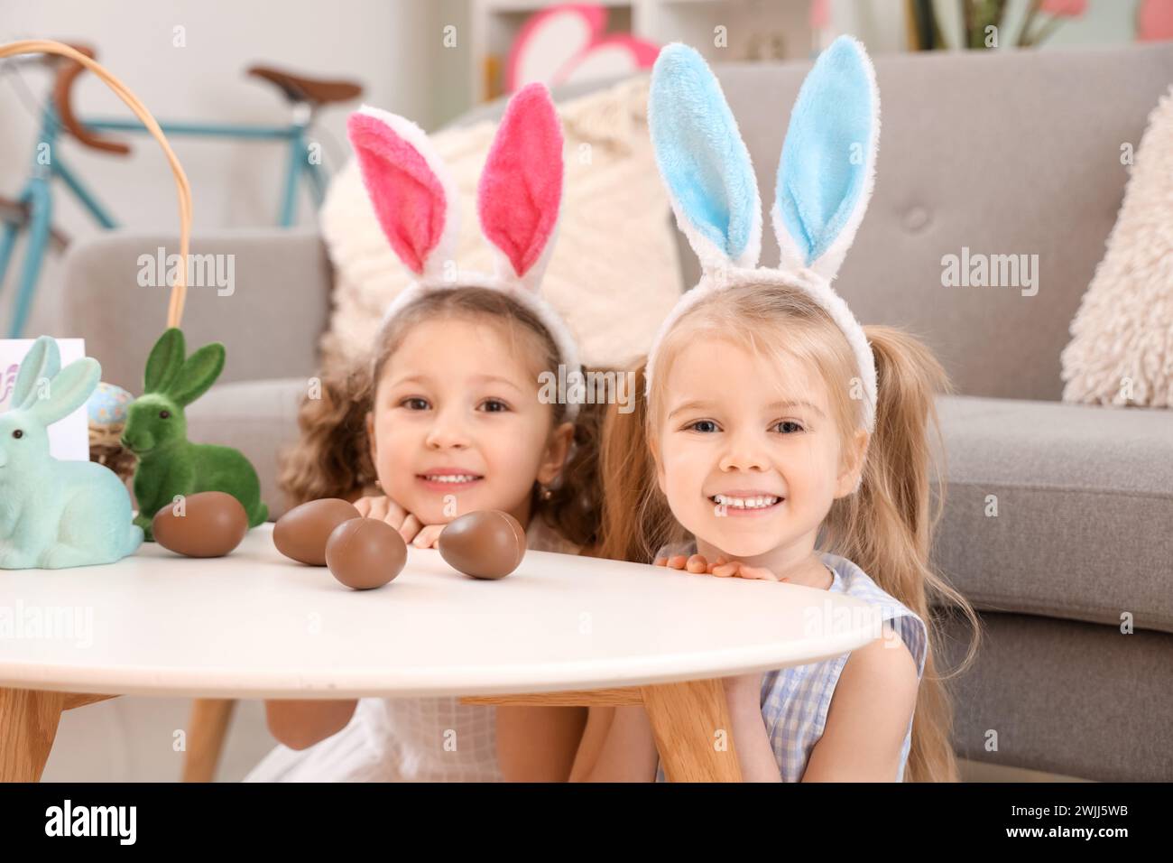 Niedliche kleine Mädchen in Hasenohren mit Schokoladen-Ostereiern auf dem Tisch zu Hause Stockfoto