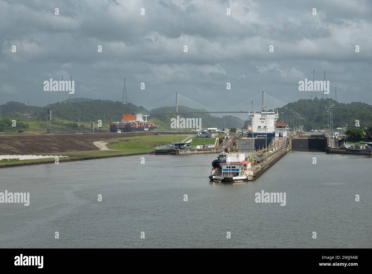 Panamakanal, Panama - 24. Juli 2023: Pedro Miguel schlängelt unter grauer Wolkenlandschaft mit Centennial Bridge, Panamerikanischer Autobahnbrücke hinten. Wide Lands Stockfoto