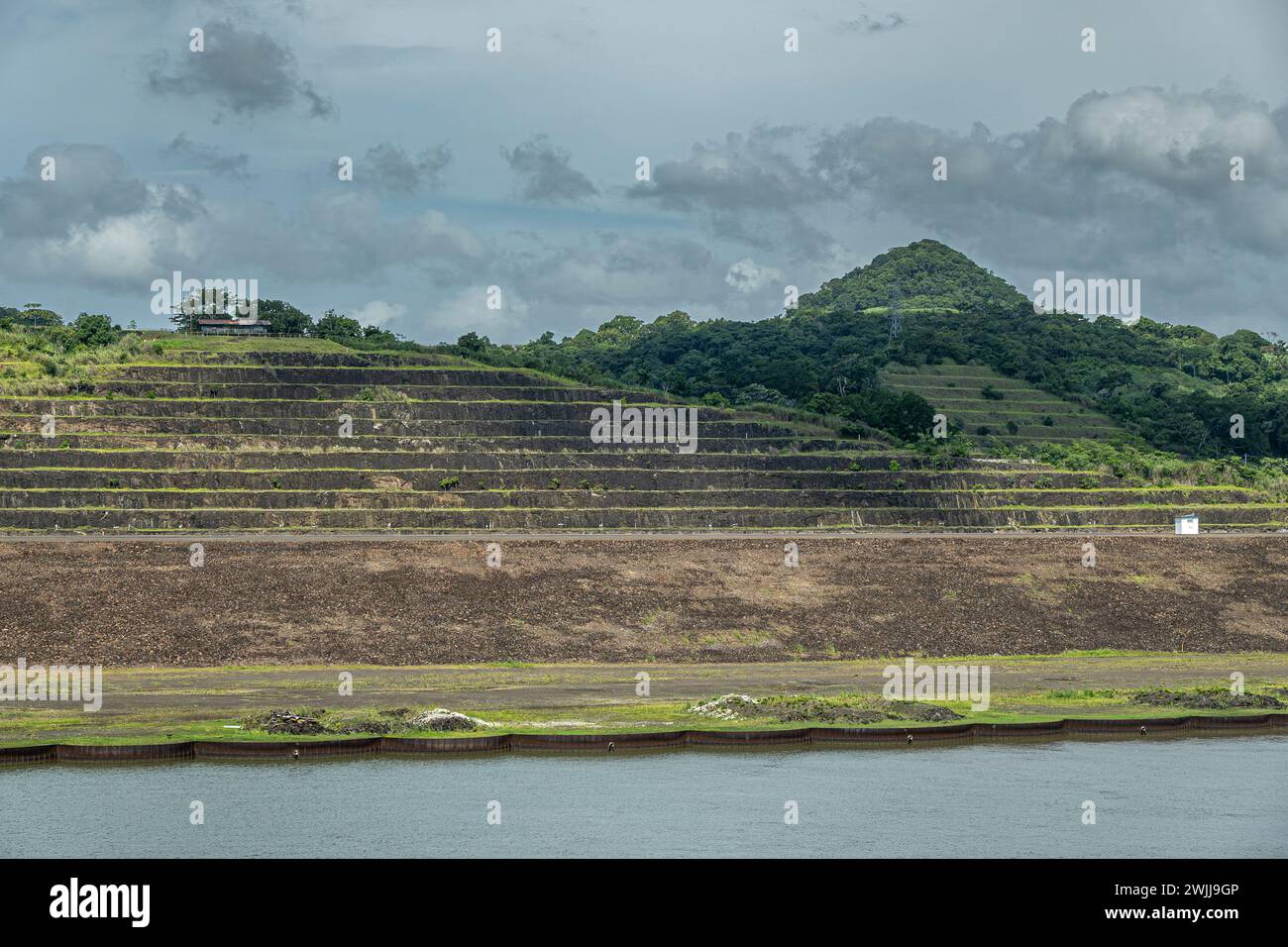 Panamakanal, Panama - 24. Juli 2023: Westküste der Pedro Miguel Schleusen mit terrassenförmig angelegtem Ackerland und bewaldetem Hügel unter blauer Wolkenlandschaft Stockfoto
