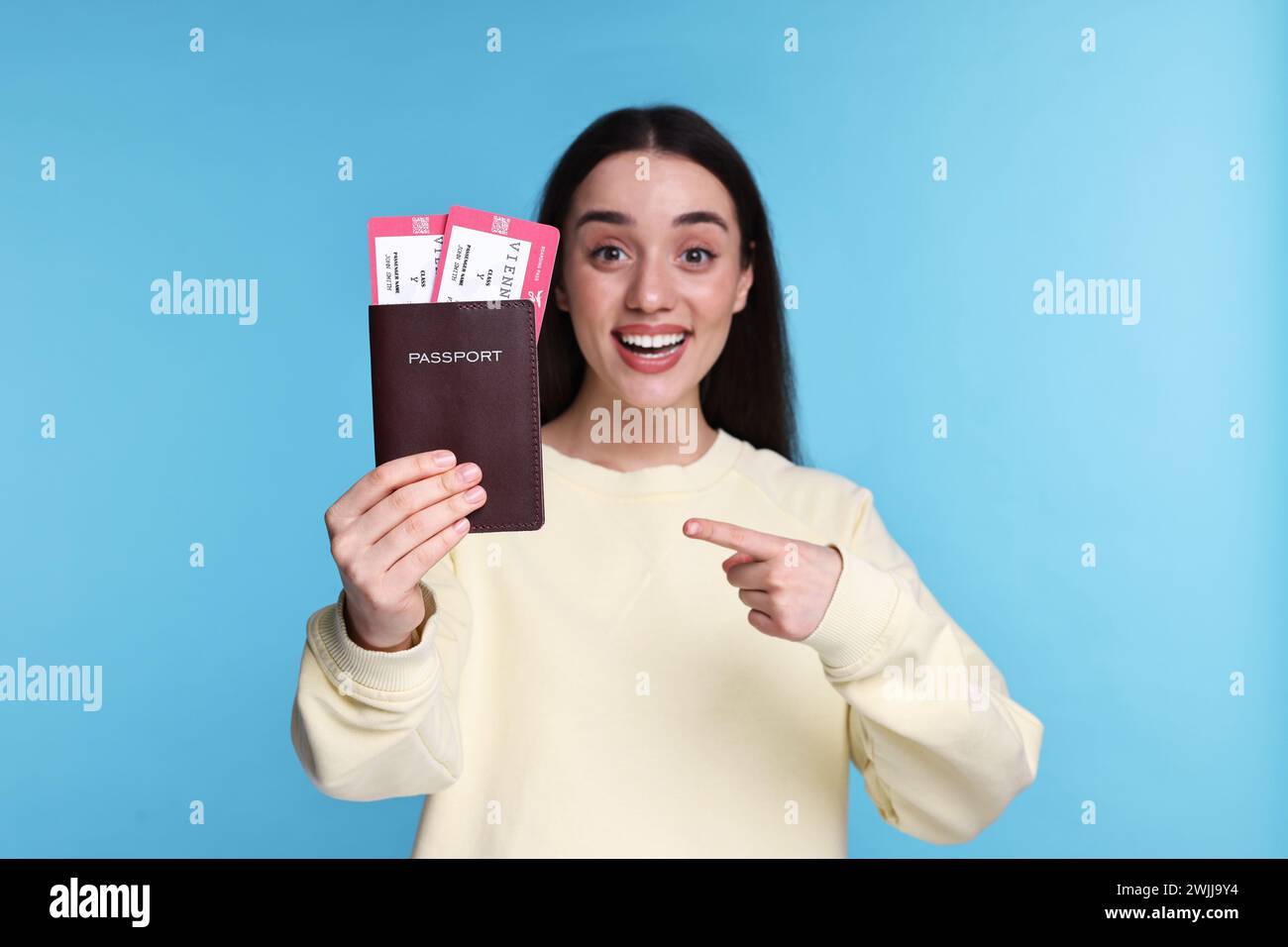 Glückliche Frau, die auf Pass und Tickets auf hellblauem Hintergrund zeigt, selektiver Fokus Stockfoto