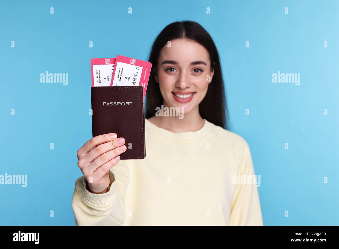 Glückliche Frau, die Pass und Tickets auf hellblauem Hintergrund zeigt, selektiver Fokus Stockfoto