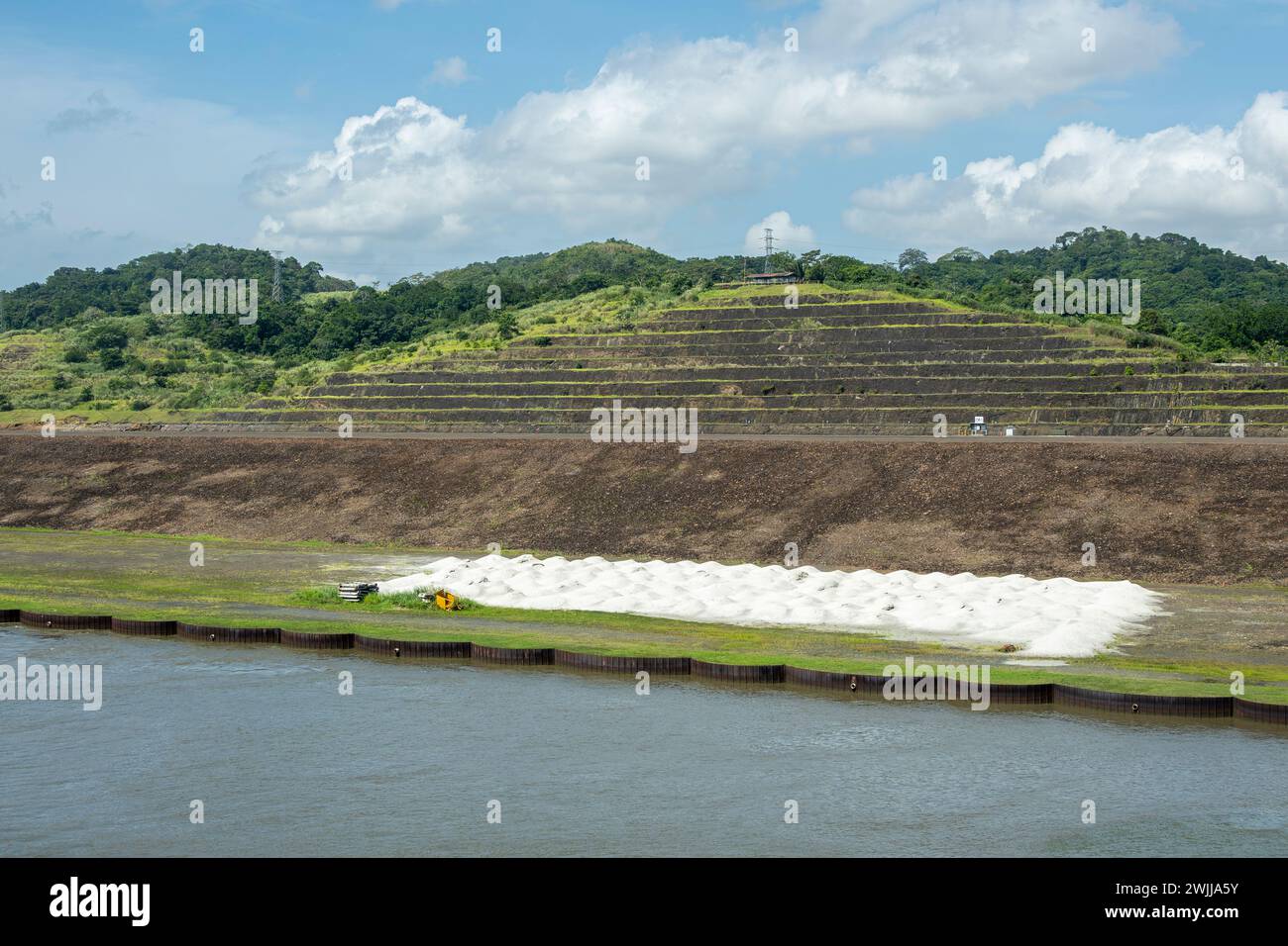 Panamakanal, Panama - 24. Juli 2023: Westküste der Pedro Miguel Schleusen mit Salzhaufen und Terrassen-Ackerland und bewaldeten Hügeln unter blauer Wolkenlandschaft Stockfoto