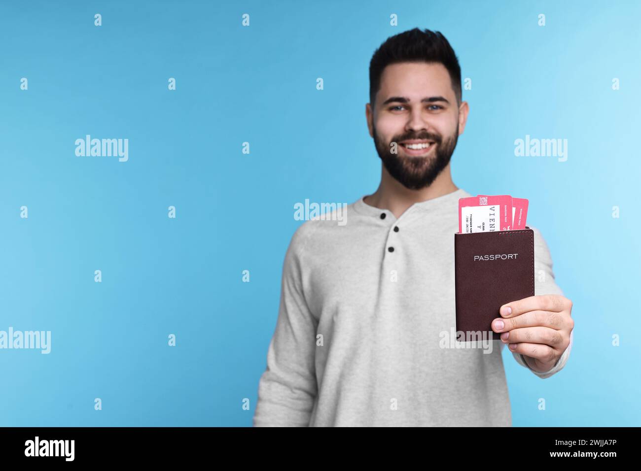 Glücklicher Mann, der Pass und Tickets auf hellblauem Hintergrund zeigt. Leerzeichen für Text Stockfoto