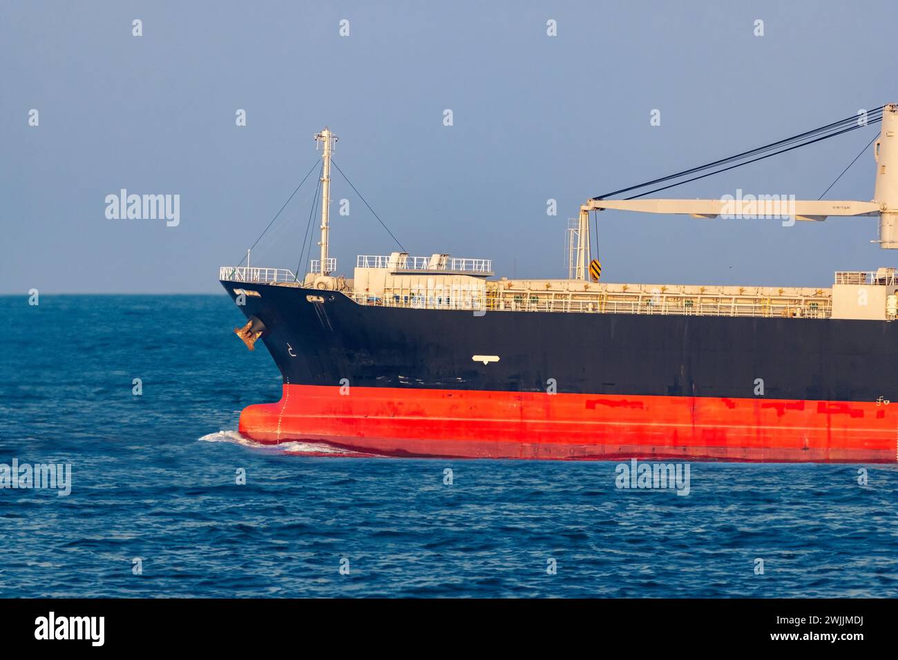 Ein Frachtschiff mit einem Kran fährt mit dem Horizont auf dem offenen Meer Stockfoto