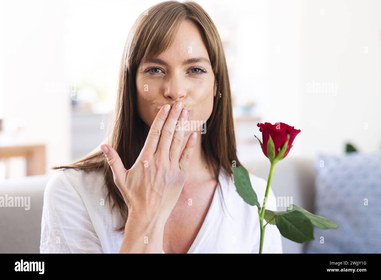 Eine junge kaukasische Frau wirft einen Kuss in die Kamera und hält eine rote Rose in der Hand Stockfoto