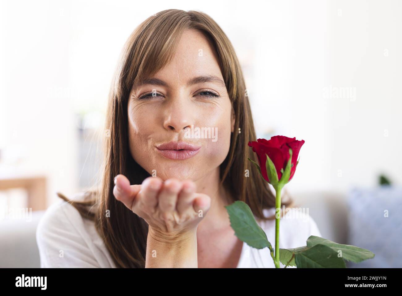Eine weiße Frau mittleren Alters bläst spielerisch einen Kuss, während sie eine rote Rose hält Stockfoto