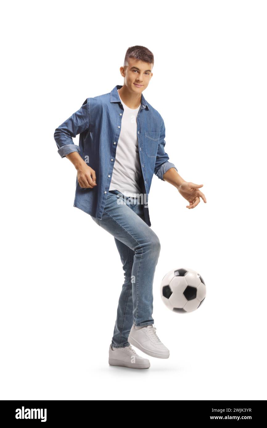 Lässiger junger Mann, der einen Fußball tritt und auf die Kamera auf weißem Hintergrund blickt Stockfoto