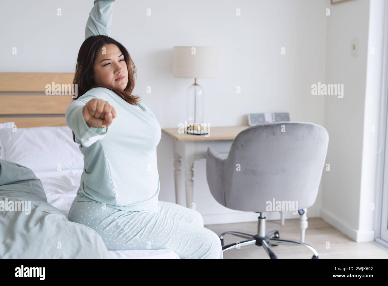 Junge birassische und große Frau dehnt sich, nachdem sie in ihrem Schlafzimmer aufgewacht ist Stockfoto