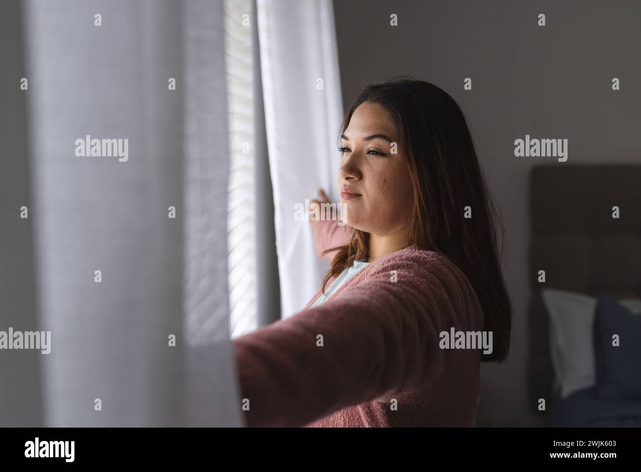 Eine junge Frau in Übergröße schaut nachdenklich zu Hause aus dem Fenster Stockfoto