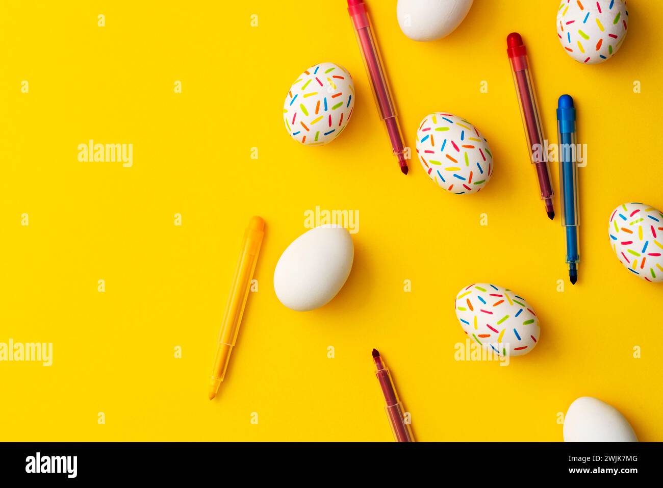 Bestreuen Sie farbige ostereier mit Farbstiften auf gelbem Hintergrund. Direkt über der Tischplatte. Stockfoto