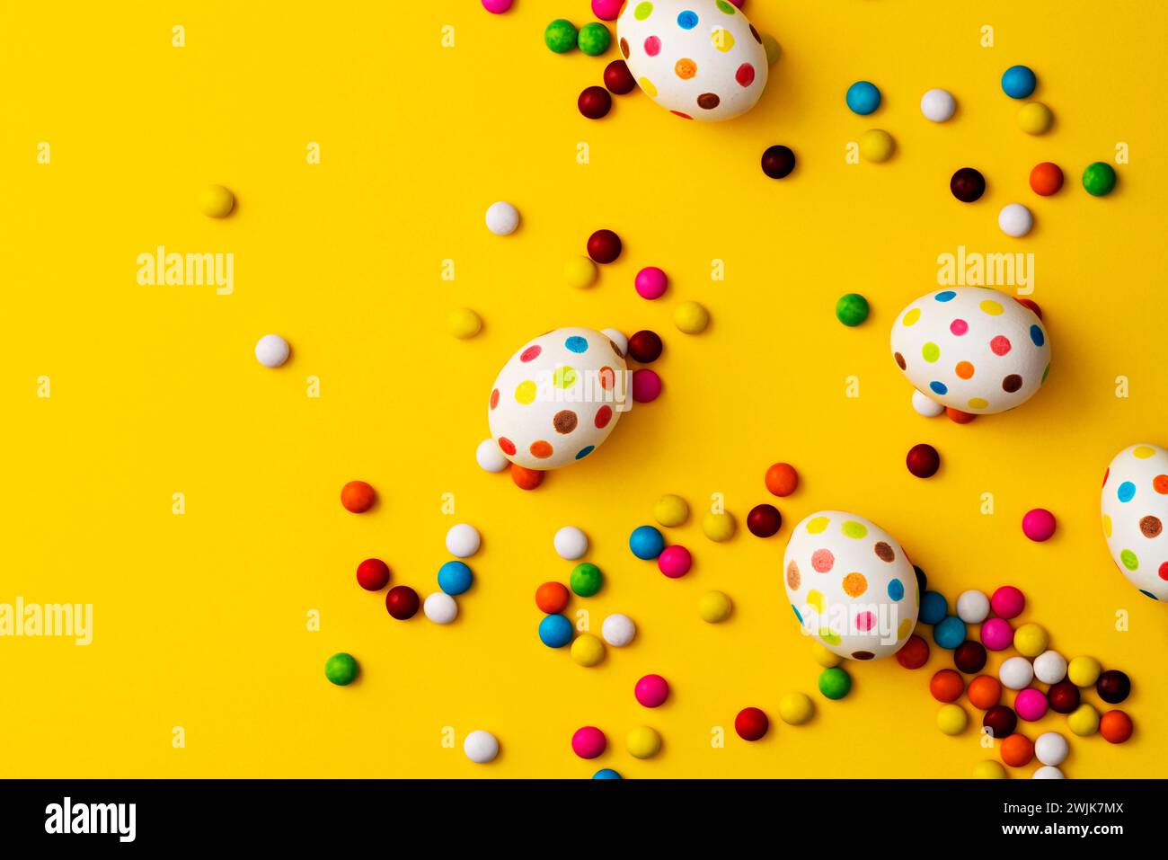 Bunte ostereier und bunte Schokoladenbohnen auf gelbem Hintergrund. Direkt über der Tischplatte. Stockfoto