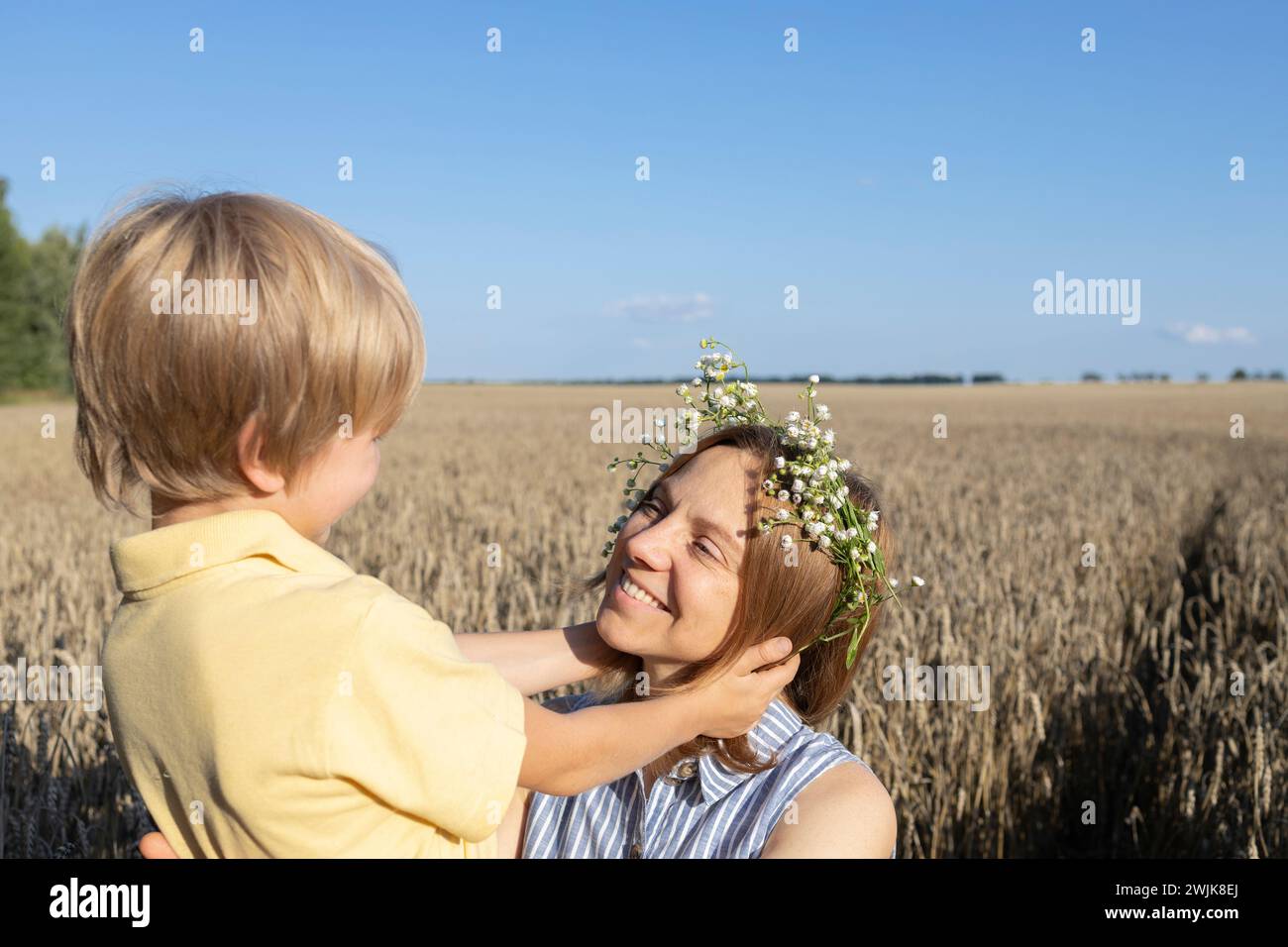 Glückliche Mutter und Sohn auf einem Weizenfeld, der Junge hält sanft den Kopf seiner Mutter. Das Konzept der elterlichen Liebe, Mutterschaft. Muttertag. Genießen Sie die Natur und das Leben Stockfoto