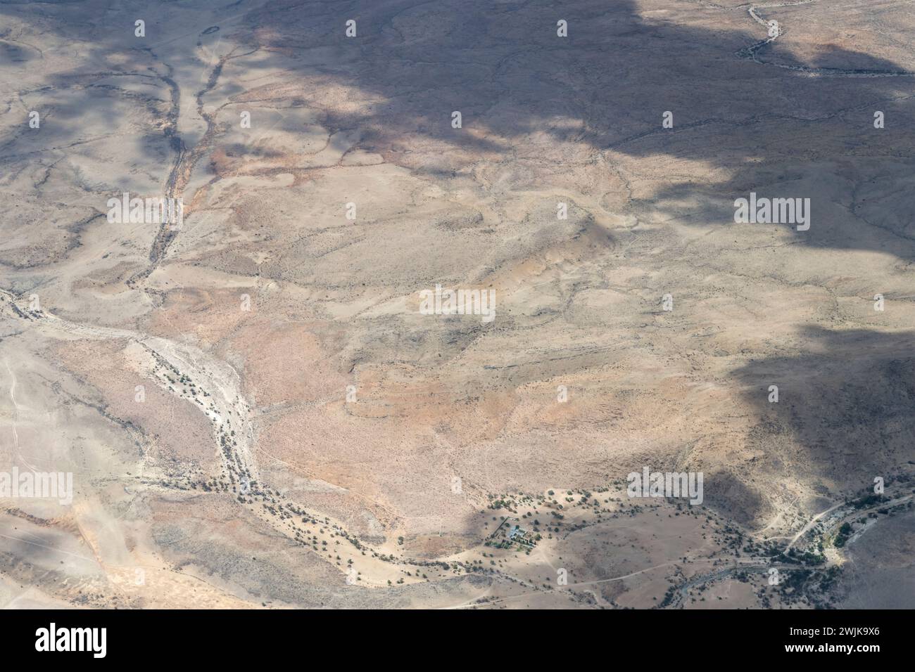 Luftlandschaft mit Bauernhof und trockenem Flussbett in hügeliger Wüste, aufgenommen von einem Segelflugzeug im hellen Licht des späten Frühlings westlich von Riethoog, Namibia, Afrika Stockfoto