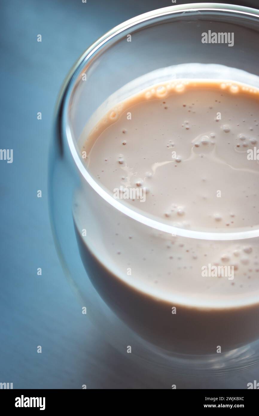 Cremiger Kaffee auf beigefarbenem Hintergrund mit Kopierraum. Milchschaum mit Espresso im Glas. Frappe im Glas auf dem Tisch in pfirsichfarbener Fuzz-Farbe. Kalter Cappuccino. Stockfoto