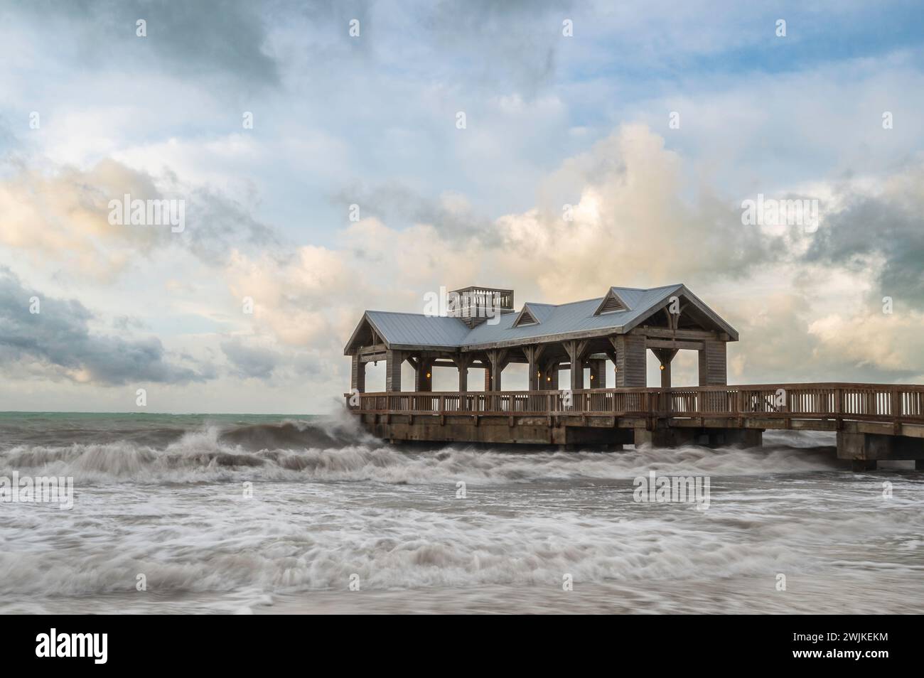Ein hölzerner Pier, mit einem überdachten Teil am Ende, der in ein abgehacktes, raues Meer reicht Stockfoto