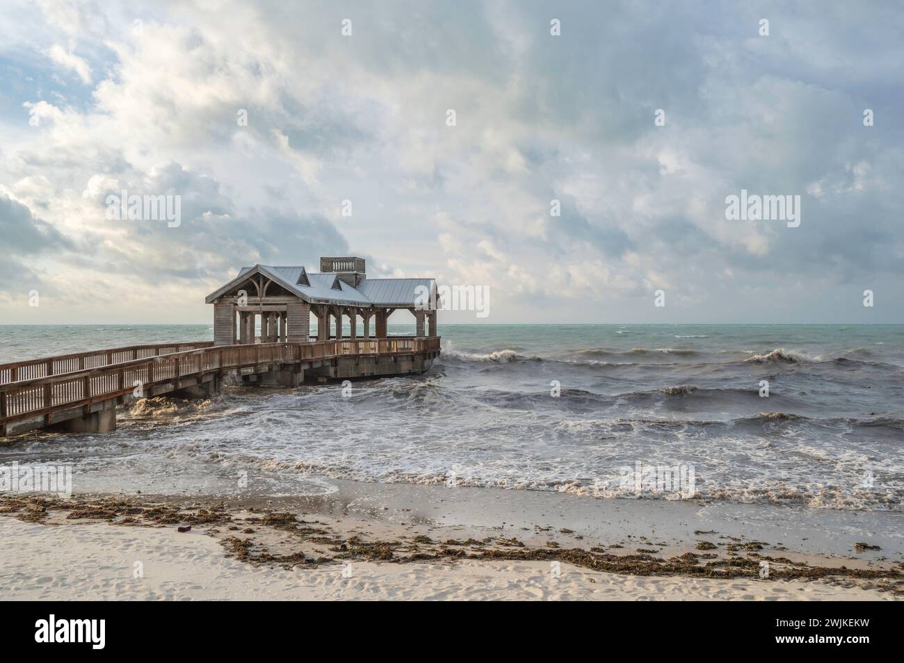 Ein hölzerner Pier, mit einem überdachten Teil am Ende, der in ein abgehacktes, raues Meer reicht Stockfoto