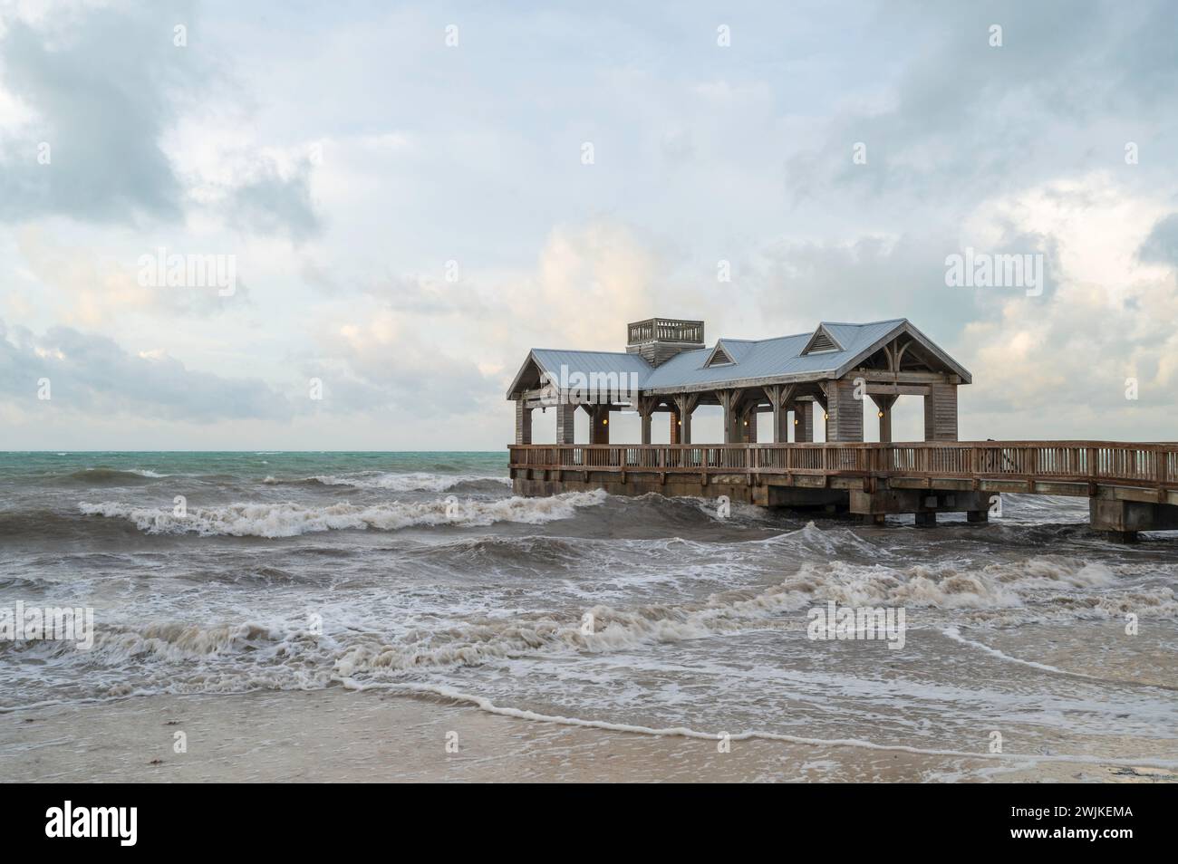 Ein hölzerner Pier, mit einem überdachten Teil am Ende, der in ein abgehacktes, raues Meer reicht Stockfoto