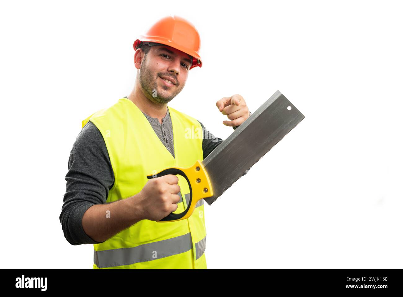 Männlicher Konstrukteur mit freundlichem, fröhlichem Ausdruck, der Zeigefinger auf Holzsäge zeigt, isoliert auf weißem Studiohintergrund Stockfoto