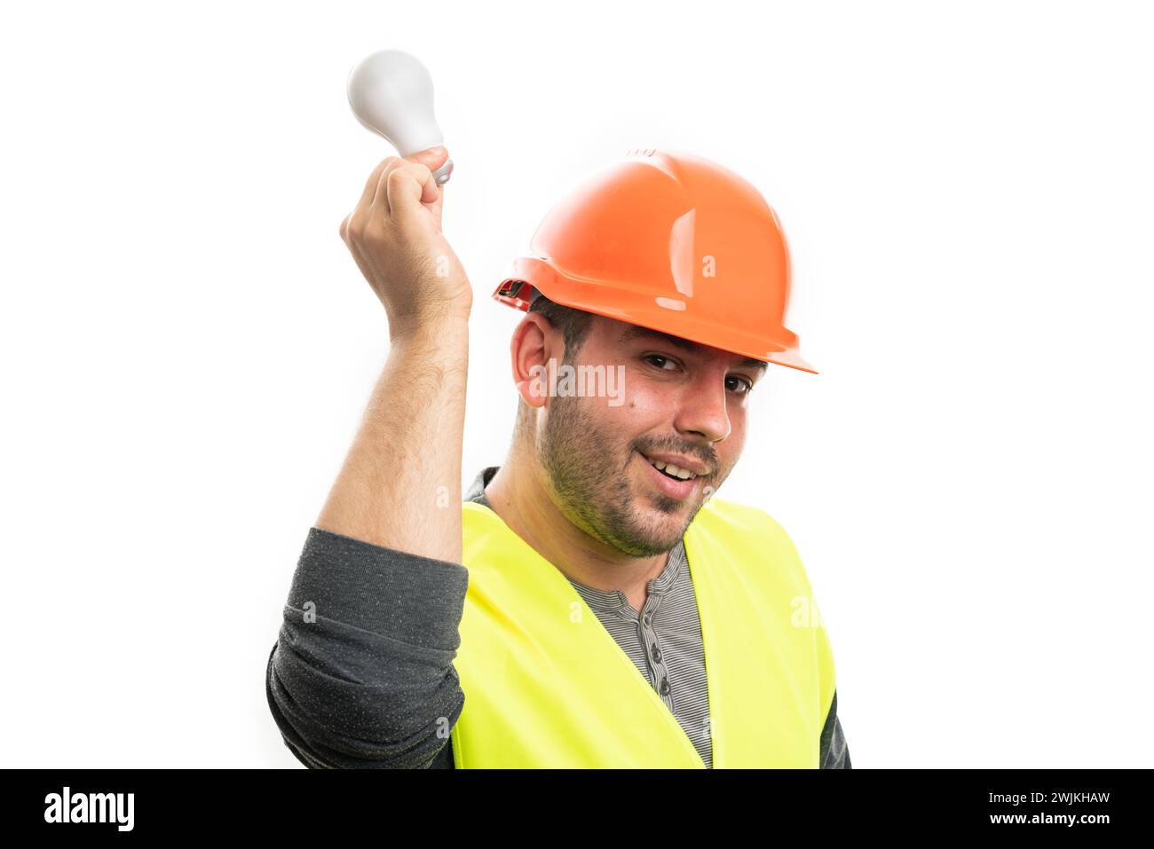 Fröhlicher erwachsener Baumeister-Mann, der Arbeitsausrüstung trägt orangefarbener Helm und gelbe Weste, die Glühbirne über dem Kopf hält, als gute helle Idee Konzept isoliert auf W Stockfoto