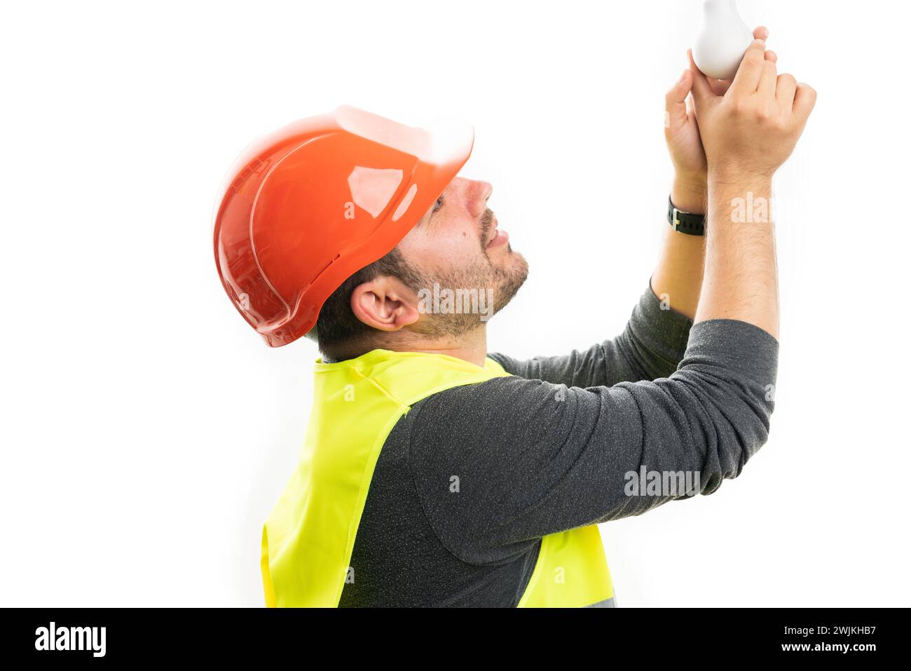 Bauarbeiter trägt orangefarbenen Schutzhelm und fluoreszierende Weste, die Glühbirne auf weißem Studiohintergrund wechselt Stockfoto
