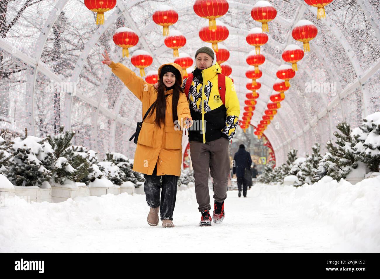 Glückliches Paar, das auf dem Hintergrund der chinesischen Neujahrsdekorationen läuft. Festliche Gasse mit roten Papierlaternen in der Winterstadt Stockfoto